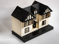 A Tudor style doll's house in the 1930s Mock-Tudor vernacular with twin jettied oriel windows and leaded glass style metal window frames.