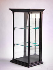 A beautifully proportioned late 19th century table-top ebonised display cabinet with glass on three sides, and with a window of glass on top - so that its contents could be lit from above. It has an elegant plinth base, a top with stepped entablature, and is fitted with three removable glass shelves. The hinged back is fitted inside with a full length mirror that is gently foxed, and it is opened and closed using a brass pull-catch. 
