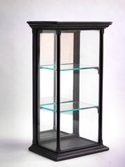 A beautifully proportioned late 19th century table-top ebonised display cabinet with glass on three sides, and with a window of glass on top - so that its contents could be lit from above. It has an elegant plinth base, a top with stepped entablature, and is fitted with three removable glass shelves. The hinged back is fitted inside with a full length mirror that is gently foxed, and it is opened and closed using a brass pull-catch. 