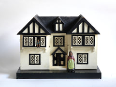 A Tudor style doll's house in the 1930s Mock-Tudor vernacular with twin jettied oriel windows and leaded glass style metal window frames.
