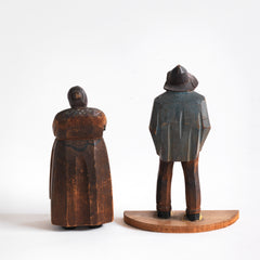 A pair of antique naive wood carved Bavarian peasant figures, one a woman and the other a man with a pipe.