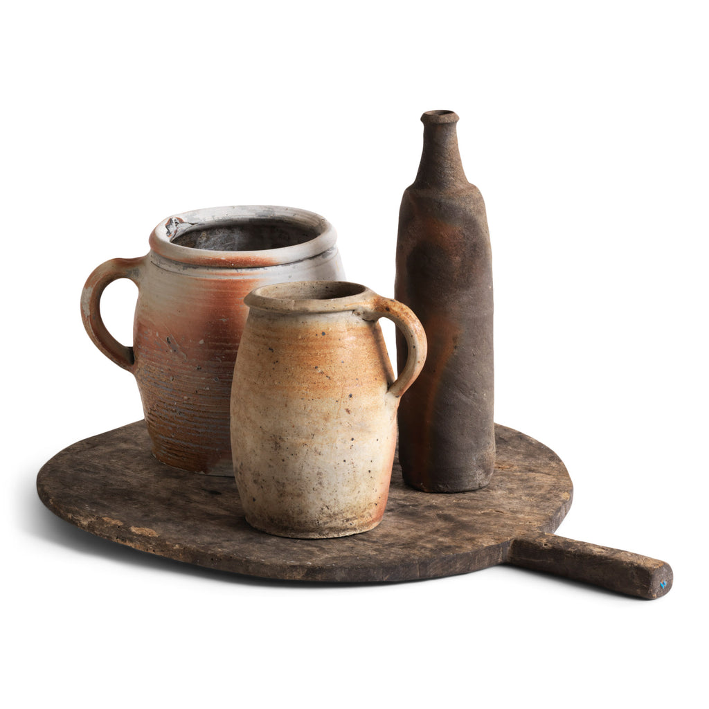 A collection of French rustic earthenware confit pots in greys, beiges and browns, and a sculptural matt moleskin brown ceramic calvados bottle. 