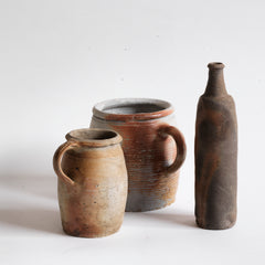 A collection of vintage French rustic earthenware confit pots in greys, beiges and browns, and a sculptural matt moleskin brown ceramic calvados bottle. 