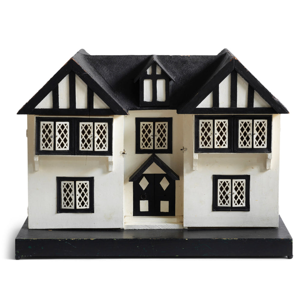 A Tudor style doll's house in the 1930s Mock-Tudor vernacular with twin jettied oriel windows and leaded glass style metal window frames.