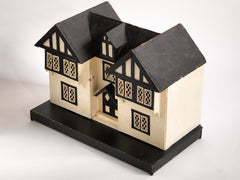 A Tudor style doll's house in the 1930s Mock-Tudor vernacular with twin jettied oriel windows and leaded glass style metal window frames.