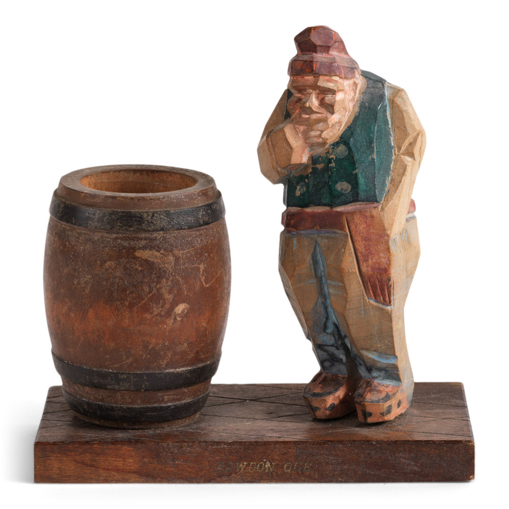 A mid twentieth century naive carved wooden figure of a contemplative rural man standing next to an open barrel.