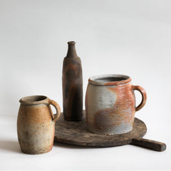 A collection of vintage French rustic earthenware confit pots in greys, beiges and browns, and a sculptural matt moleskin brown ceramic calvados bottle. 