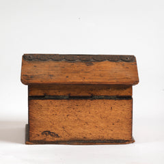 Back view of a vintage naive model wooden house savings box that resembles a Scottish bothy, with metal trim to its roof, along with metal windows and front door.