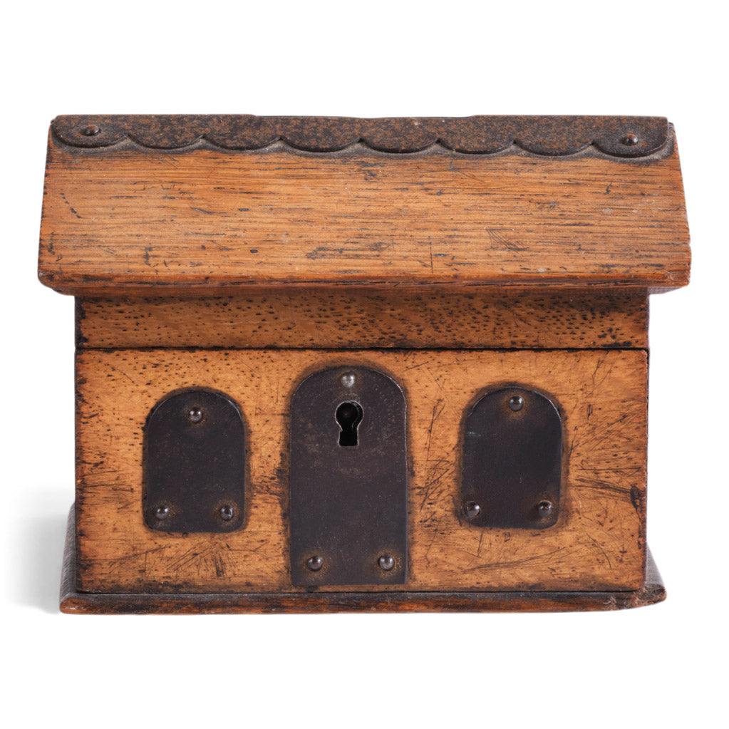 A vintage naive model wooden house savings box that resembles a Scottish bothy, with metal trim to its roof, along with metal windows and front door.