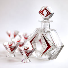 A stunning and rare Art Deco etched black and ruby glass decanter set designed by Karl Palda c.1930. The set comprises of a decanter with stopper and six conical shaped facet cut glass cocktail glasses, each with a flaring foot. Each piece is decorated with Art Deco geometric florals and red chevrons.
