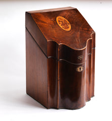 A handsome George III mahogany veneered knife box with a flower basket oval inlay on its slanting lid; a serpentine front banded in satinwood; and a compass star decoration with rope cross-banded inlay applied to the underside of its lid. The base is felt baize covered, and it has a copper escutcheon and lid pull. 