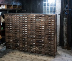 An exceptional bank of antique wooden workshop drawers with original patina and finish. Each of the 90 drawers has a cup-shaped metal pull handle and a name-plate holder; the lower, deeper drawers are singular inside, whereas the upper slimmer drawers contain divisions.