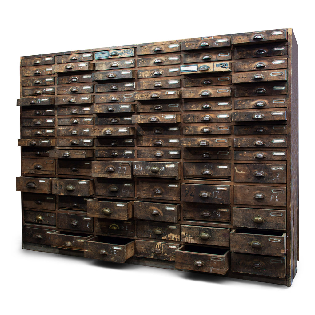 An exceptional bank of 90 wooden workshop drawers with original patina and finish. Each drawer has a cup-shaped metal pull handle and a name-plate holder; the lower, deeper drawers are singular inside, whereas the upper slimmer drawers contain divisions.