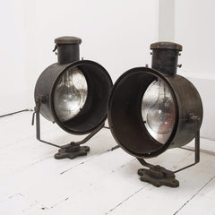 An impressive pair of early twentieth century stage lights, fitted with mercury glass reflectors, and with their original paint finish. Each light's steel housing swivels on a half-octagonal arm that is fitted with a bracket, affording the lights to be either wall or floor mounted. A side lever locks the lamp's desired angle in place.