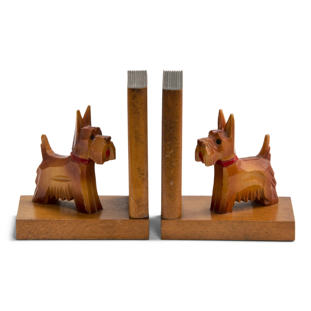 A charming pair of 1930s carved wood scottie dog bookends. Each dog has a painted red collar and tongue, and is mounted on an oak platform with an oak support modelled as a book. Scottie dogs were all the rage in the 1930s: as pets with box-clipped muzzles; as stylised Art Deco Bakelite brooches and clasps; adorning greetings and postcards; as ornaments, modelled in china, metal and wood; and as bookends - such as this dear little pair.