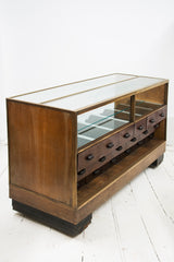 A rare high quality 1930s Art Deco shop counter fitted with eighteen Bakelite display drawers and brass frame to its vitrine. It has oak veneer panelled sides and front with black painted Art Deco stepped feet mounted on ball castors – so it can be moved with absolute ease.  The maker and shopfitters nameplate ‘Courtney Pope Ltd of London N15’ is secured to the inside front of the cabinet, and each Bakelite drawer is beautifully monogrammed with the initials CP in a striking 1930s modernist font. 