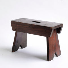 A handsome stained pine foot stool with central hand-grip to its seat and flaring uprights.