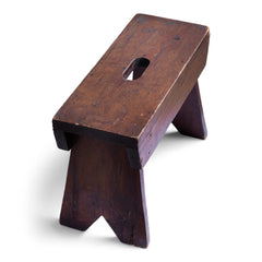 A handsome antique stained pine foot stool with central hand-grip to its seat and flaring uprights.