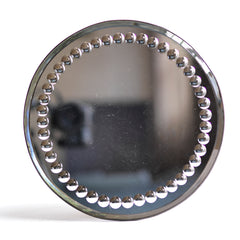 A large and very striking late 19th century tabletop circular mirror with a border of convex fish-eye inclusions, a bevelled edge and a fine metal trim. It has a cream painted back and stands of on three bun feet. 