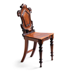 A stunning mid 19th century hall chair of fine quality mahogany having acquired good colour and patination over its 150 plus years. Its heraldic-shaped back is lusciously carved from a single piece of mahogany, with organic scrolls and fluid acanthus leaves, which frame a central shield. It has a panelled seat which stands on beautifully turned front legs, with saber-shaped legs at the rear. 