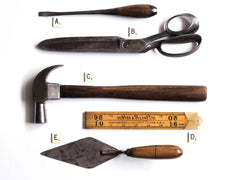 A collection of handmade vintage and antique tools, including a screw driver, tailors shears, claw hammer, carpenters rule and a trowel.